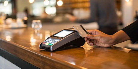 A hand holding a credit card at a terminal, part of the cost to accept payments.